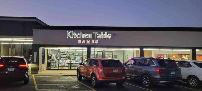 The Kitchen Table Games storefront at dusk, sign lit above the windows